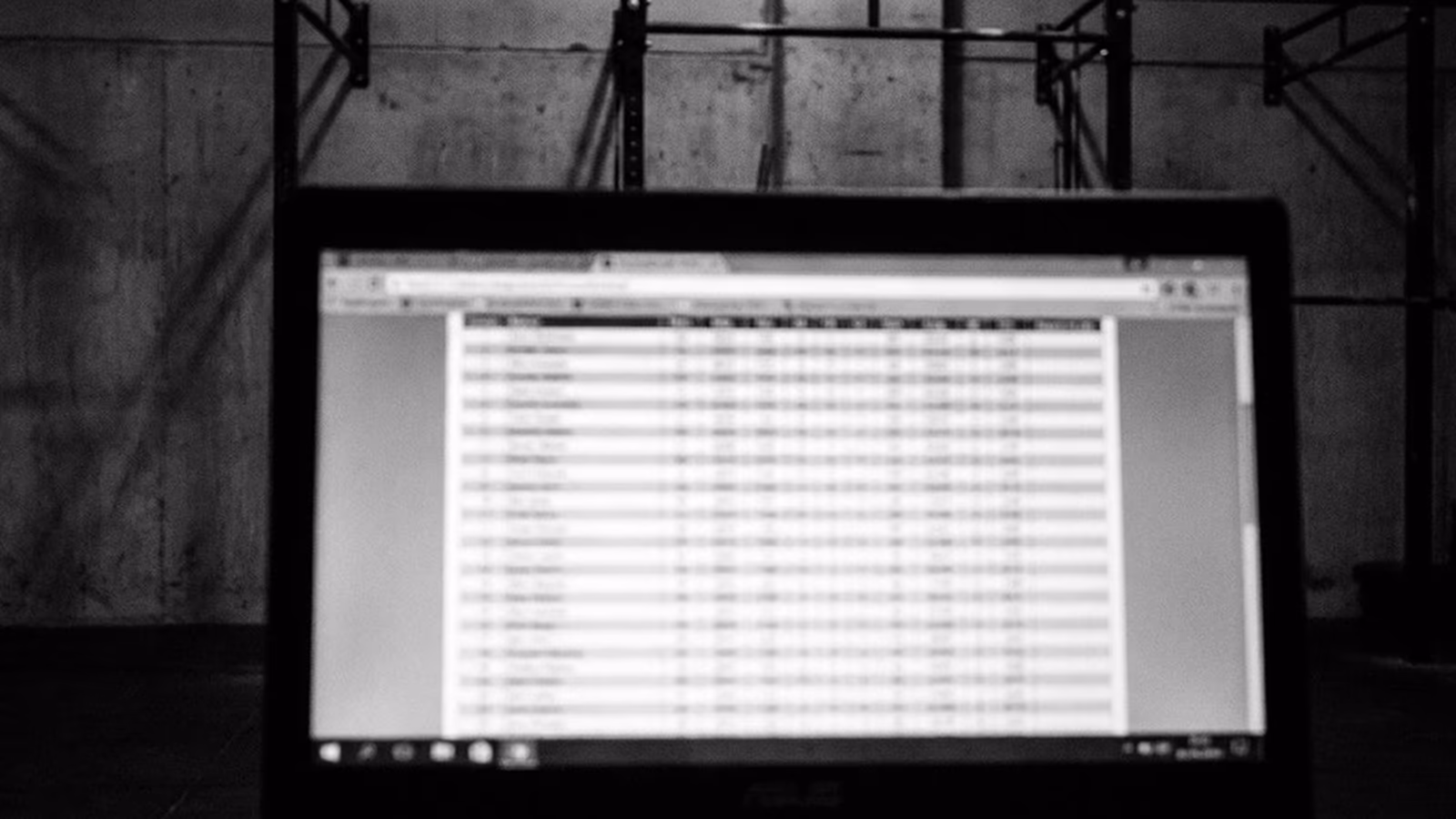 Primer plano desaturado de una pantalla de ordenador mostrando un leaderboard de CrossFit Open con filas borrosas.