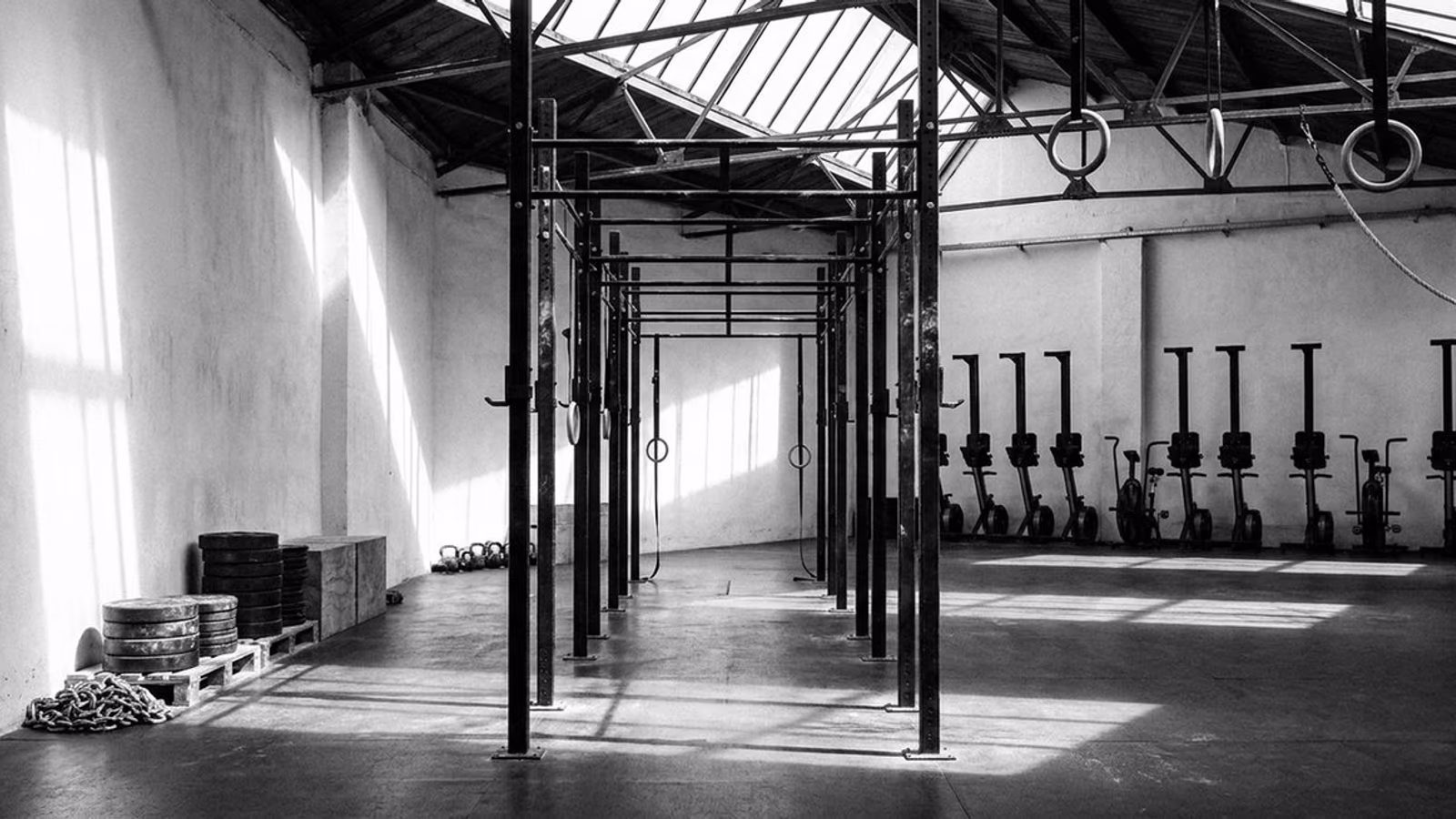 Gimnasio abierto con paredes blancas encaladas, cuatro rigs paralelos y una fila de bicicletas de asalto al fondo.